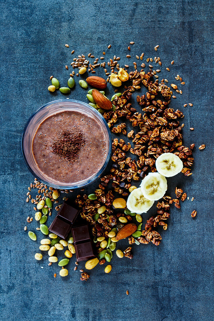 Delicious banana chocolate smoothie with homemade granola, nuts and seeds on dark vintage backdrop