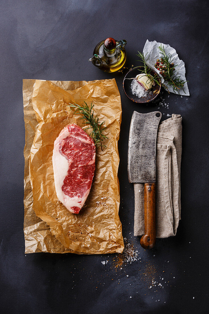 Rohes Striploin Steak mit Salz, Pfeffer, Gewürzen, Öl und Fleischerbeil