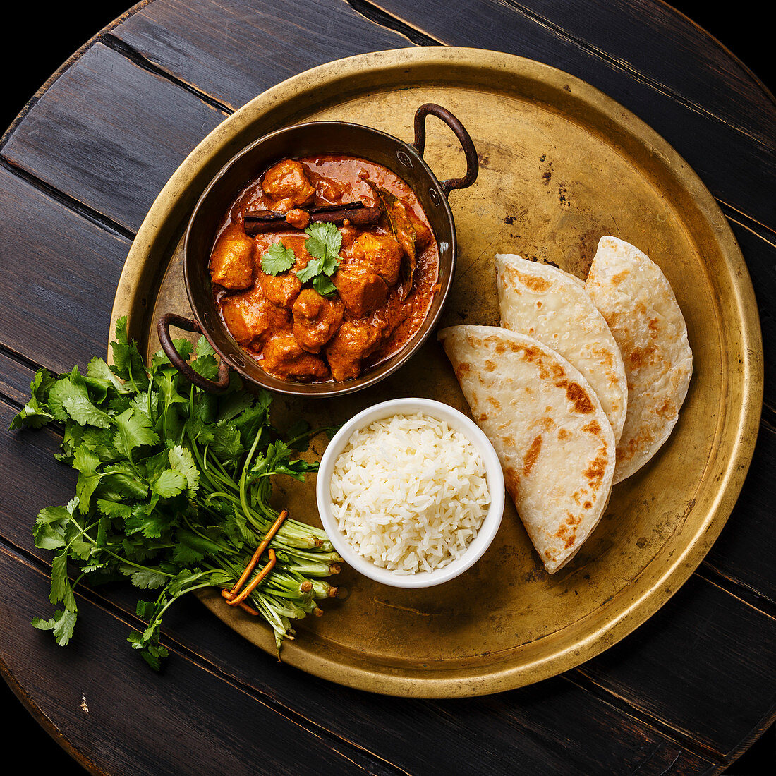 Chicken tikka masala spicy curry meat food with rice and naan bread on copper tray on wooden background