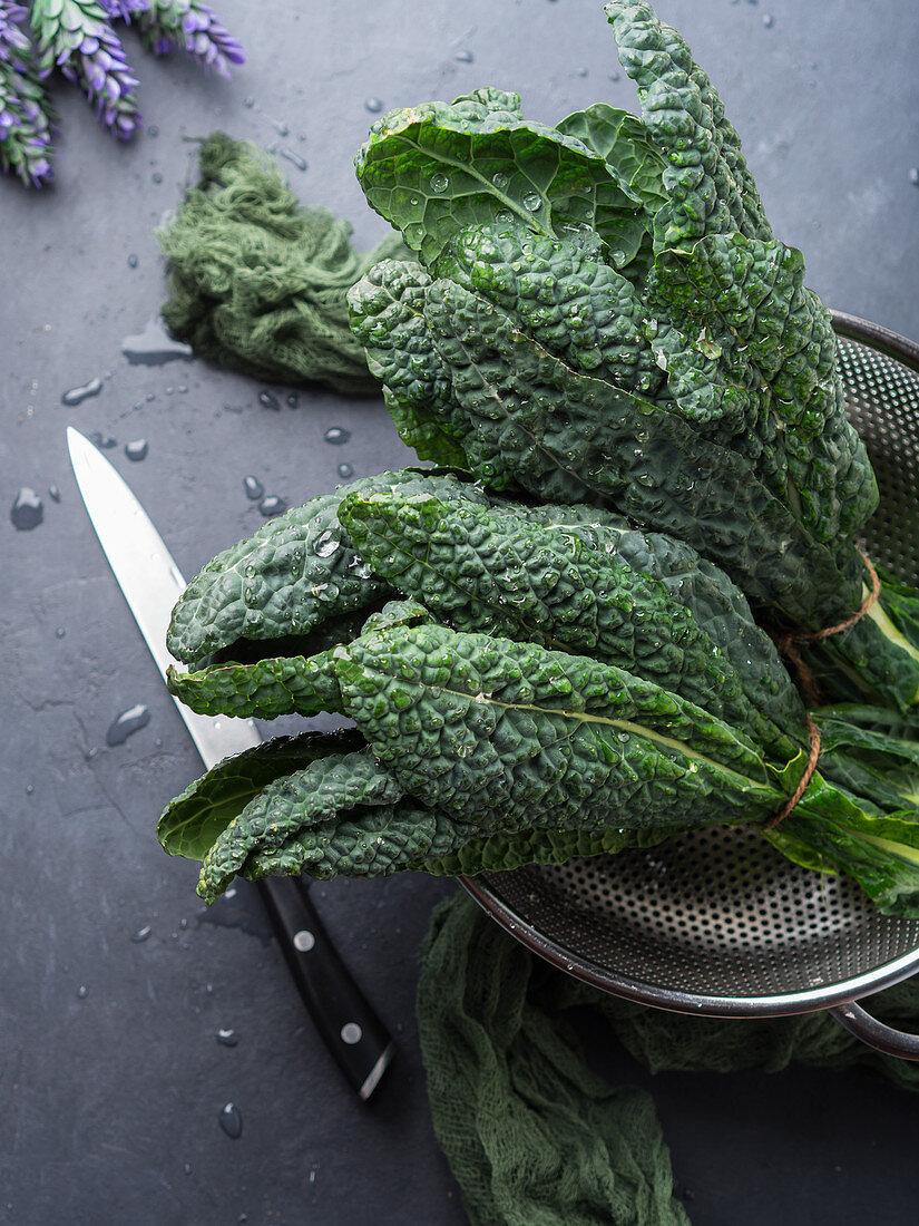 Black (Tuscan) kale in a colander over black background