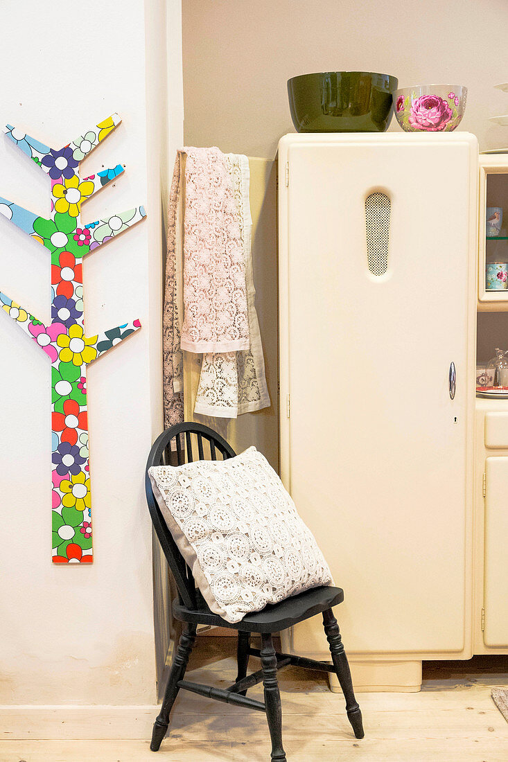 Stylised plywood tree covered with colourful foil, cushion on chair and cream fridge