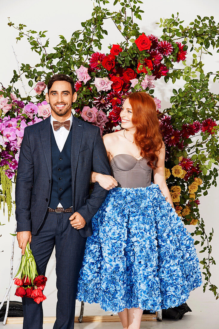 A red-haired woman wearing a blue-and-white skirt with a bodysuit and a dark-haired man wearing a suit