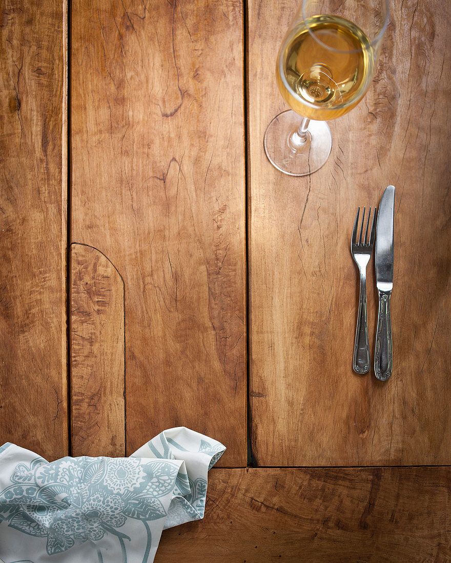 Besteck und ein Glas Weißwein auf Holztisch