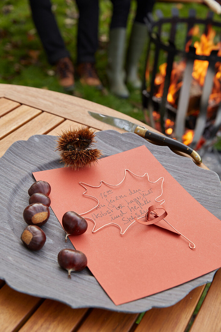 An homemade autumnal invitation on a wooden platter with chestnuts