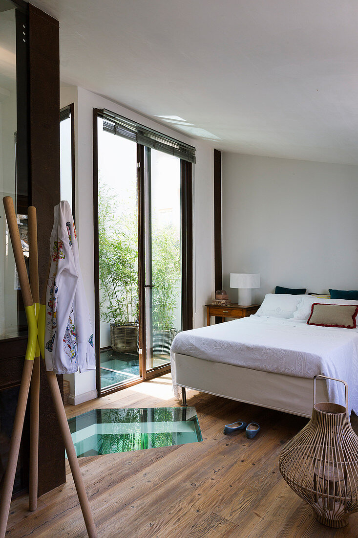 Doppelbett, Holzdielenboden mit Glaseinsatz und offene Balkontür im Schlafzimmer