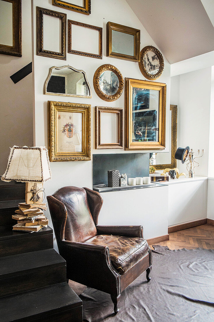 Vintage Ledersessel auf Tierfell, Tischleuchte auf Treppe und verschiedene Bilderrahmen an der Wand