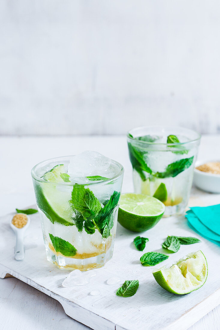 Two glasses with classic mojito, lime wedges and mint leaves on a white wood cutting board