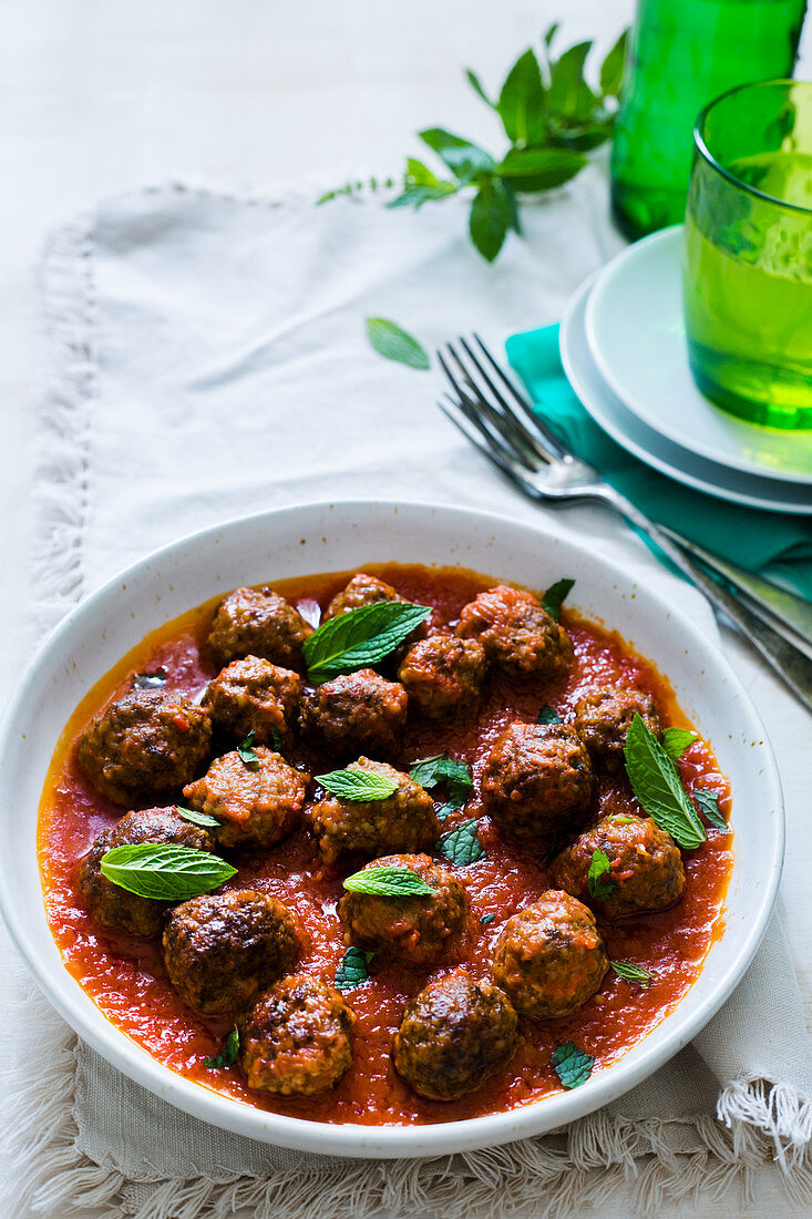 A plate with greek lamb kofta in tomatoe sauce with mint leaves