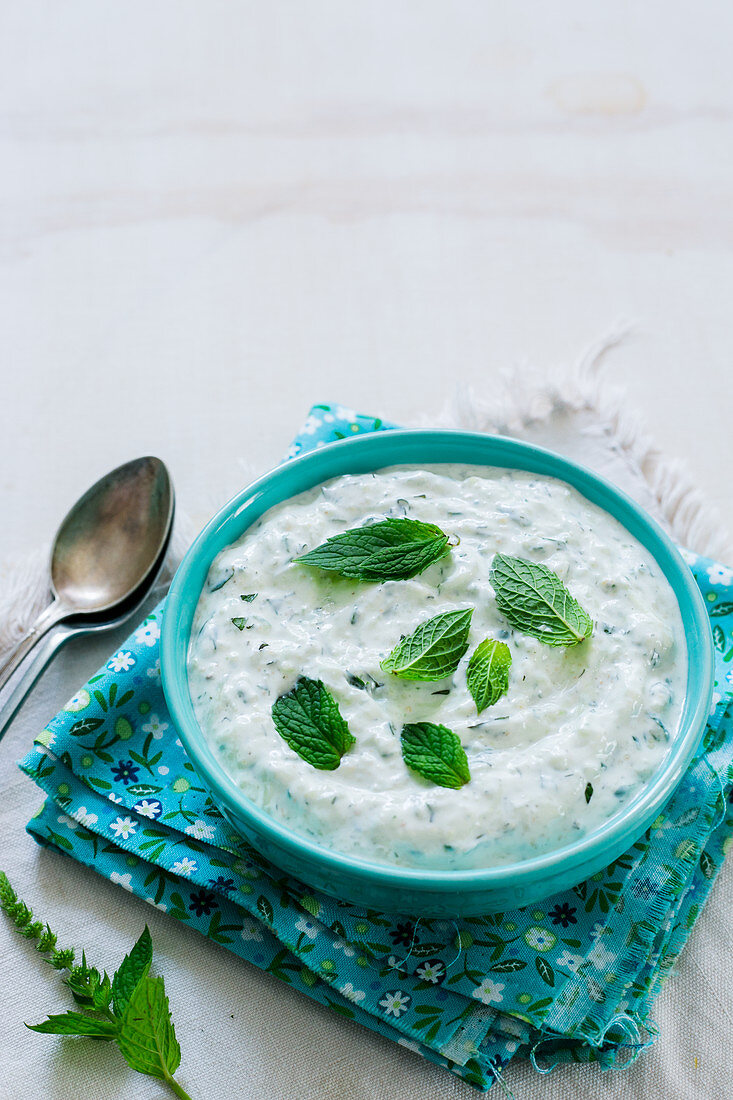 A turquoise bowl containing yogurt and mint sauce
