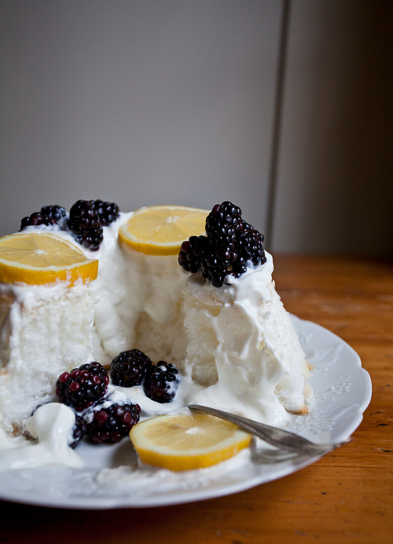 Angel food cake with whipped cream, lemon slices and blackberries