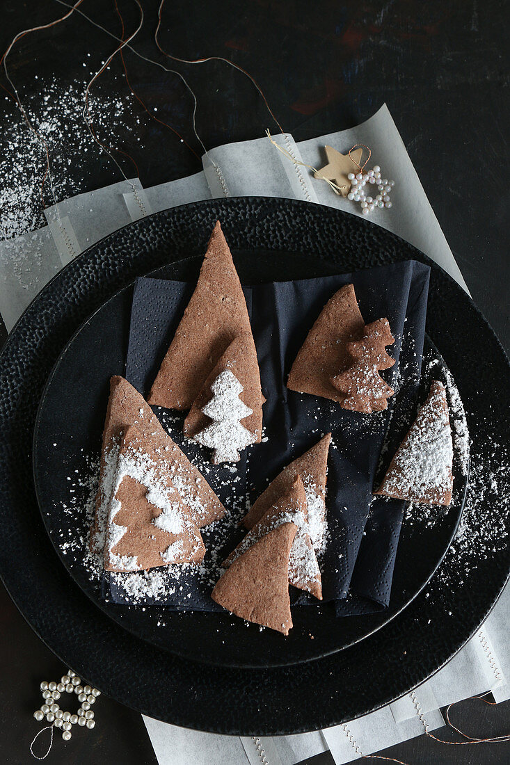 Glutenfreie Schokoladenplätzchen in Form von Dreiecken und Tannenbäumen mit Puderzucker zu Weihnachten