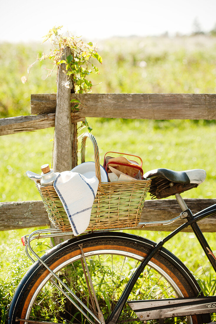 Fahrrad mit Picknickkorb an einem Holzzaun auf der Wiese