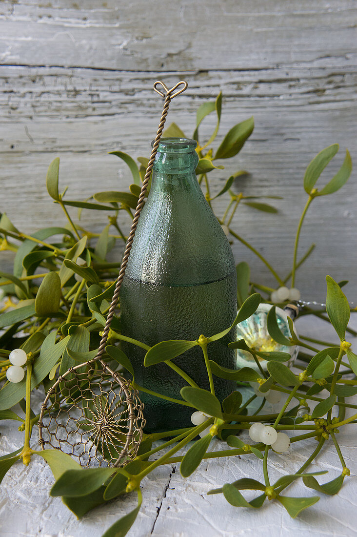 Hot damson water in a green bottle surrounded by mistletoe and a vintage sieve