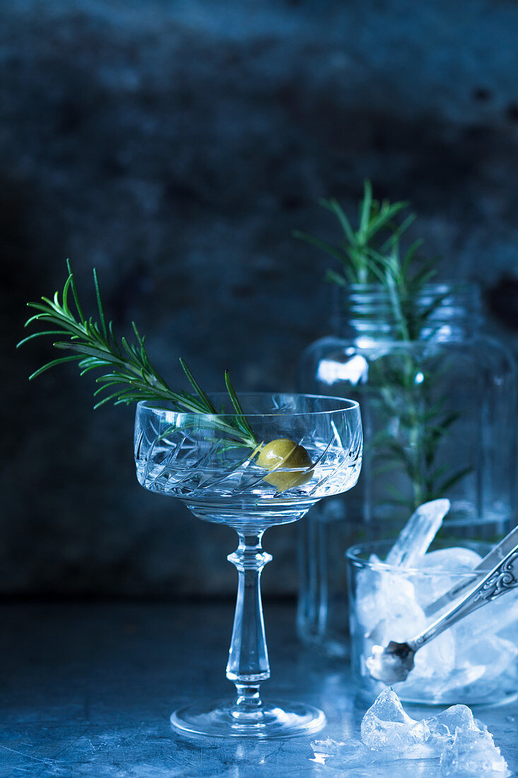 A drink garnished with an olive and a sprig of rosemary