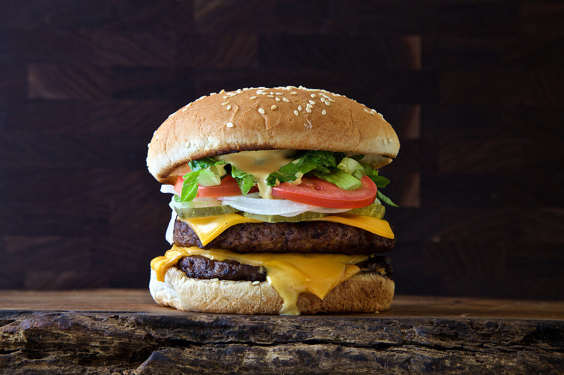 Double Burger with american cheese, lettuce and tomato on on a dark rustic background