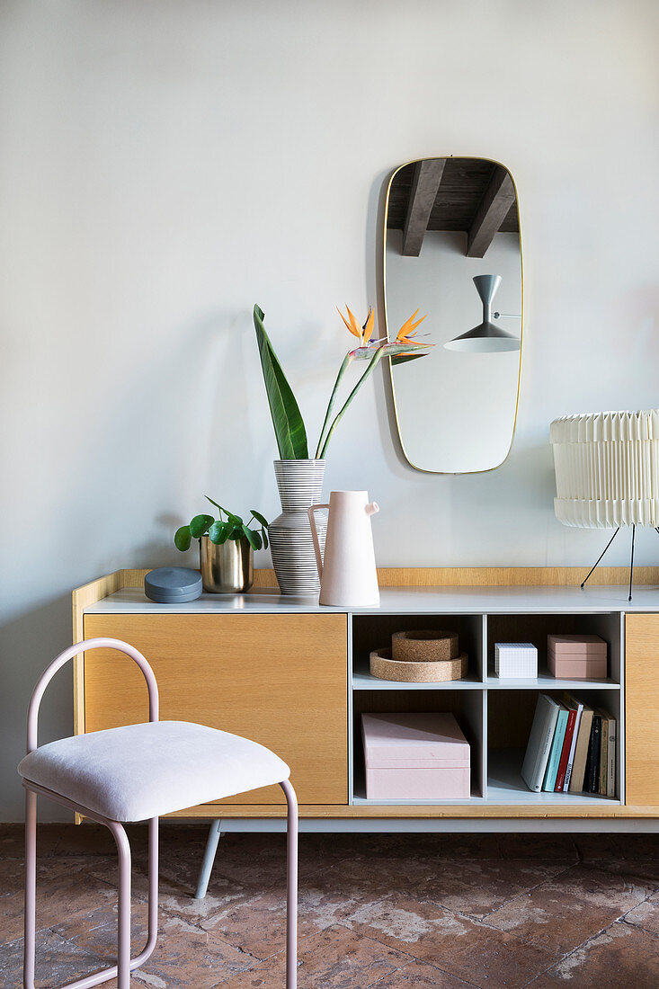 Rosafarbener Metallstuhl vor einem Sideboard mit offenen Fächern