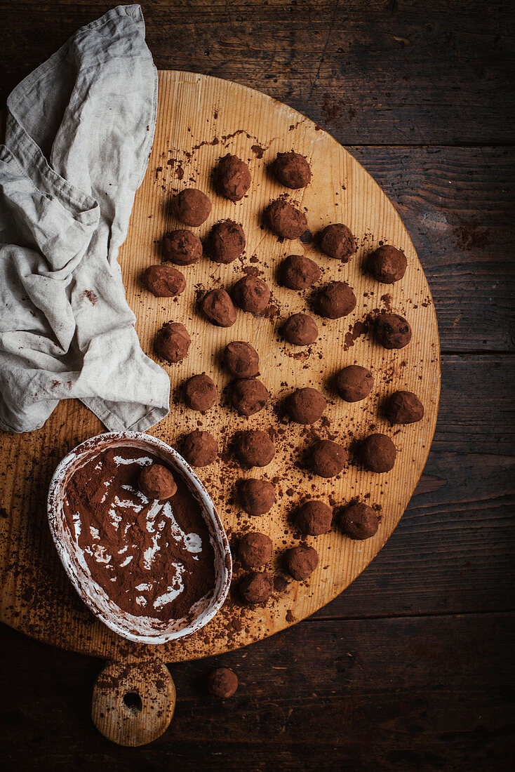 Home-made chocolate truffles dusted with cocoa powder on a wooden board (seen from above)