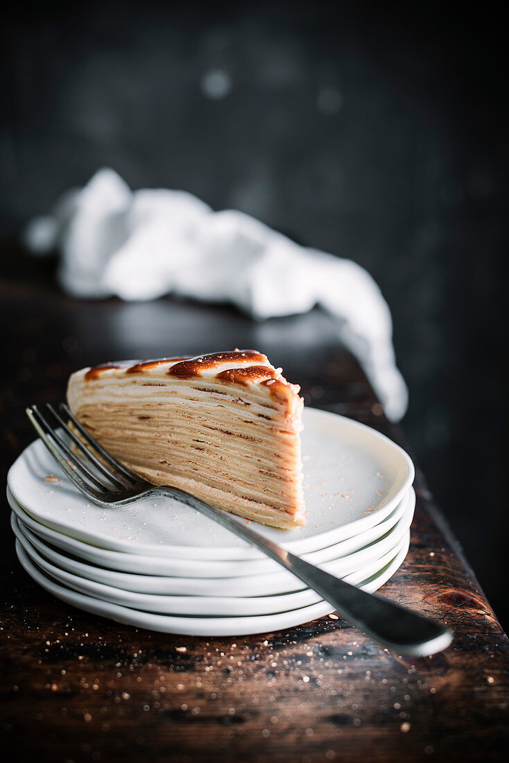 A slice of pancake cake with caramel on a stack of plates