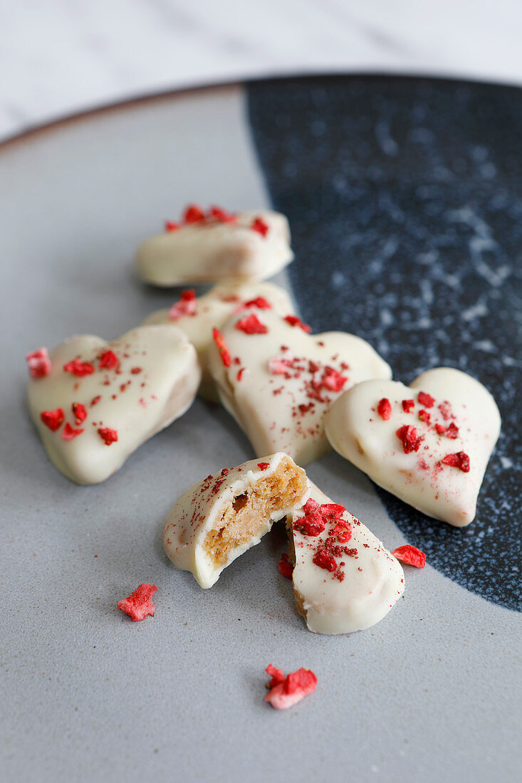 Herzförmige Kekse mit weisser Schokoladenglasur, gefriergetrockneten Erdbeeren und Glitter