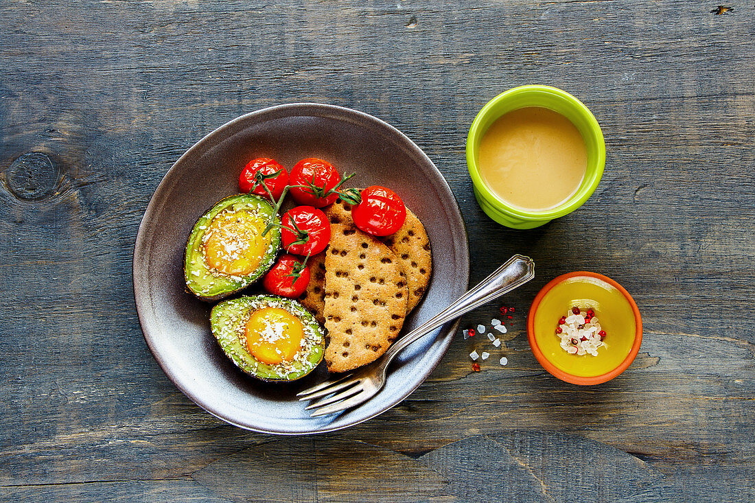 A healthy breakfast: avocado with eggs served with crackers, tomatoes and coffee