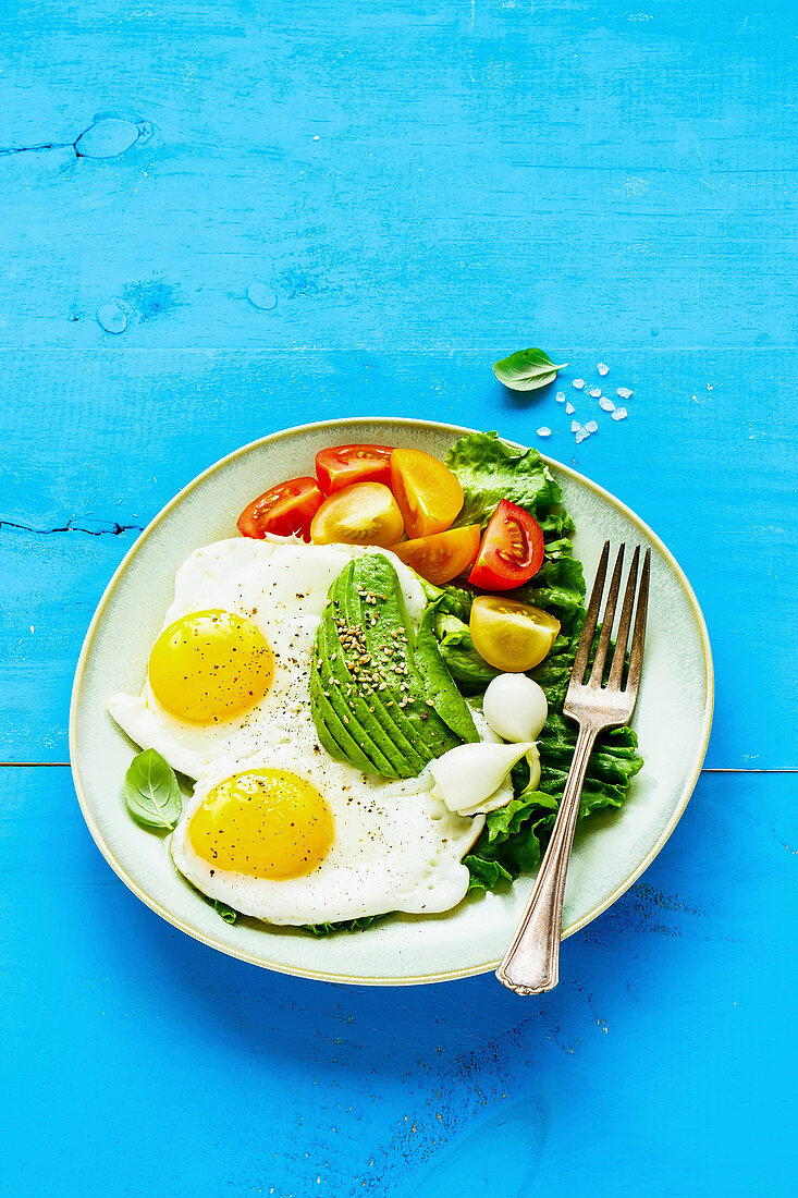 A healthy breakfast with fried eggs, avocado, tomatoes and lettuce