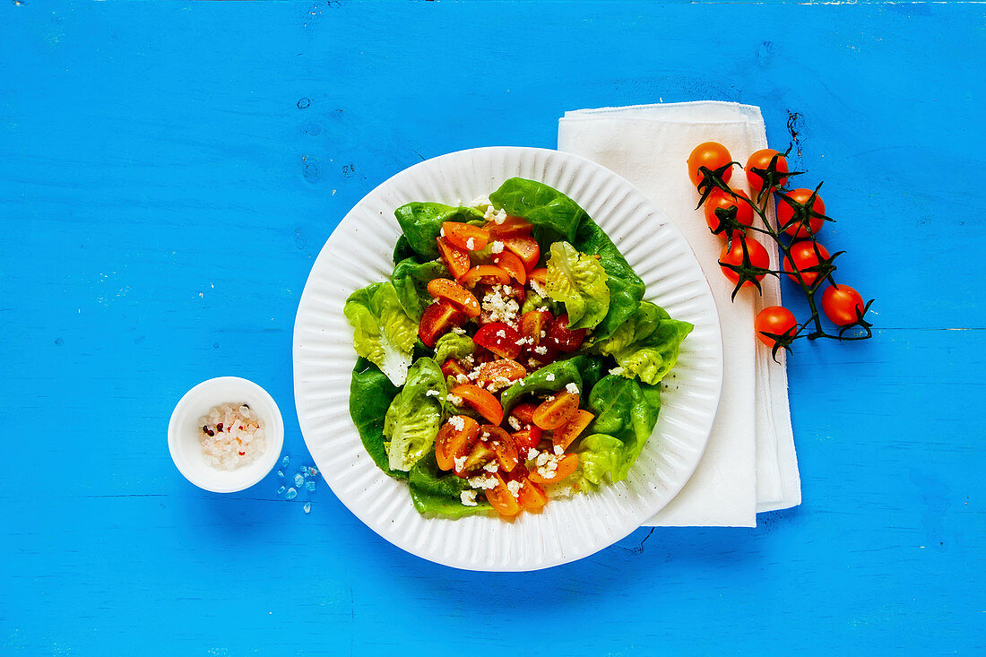 A mixed leaf salad with cherry tomatoes and feta cheese on a blue surface (seen from above)