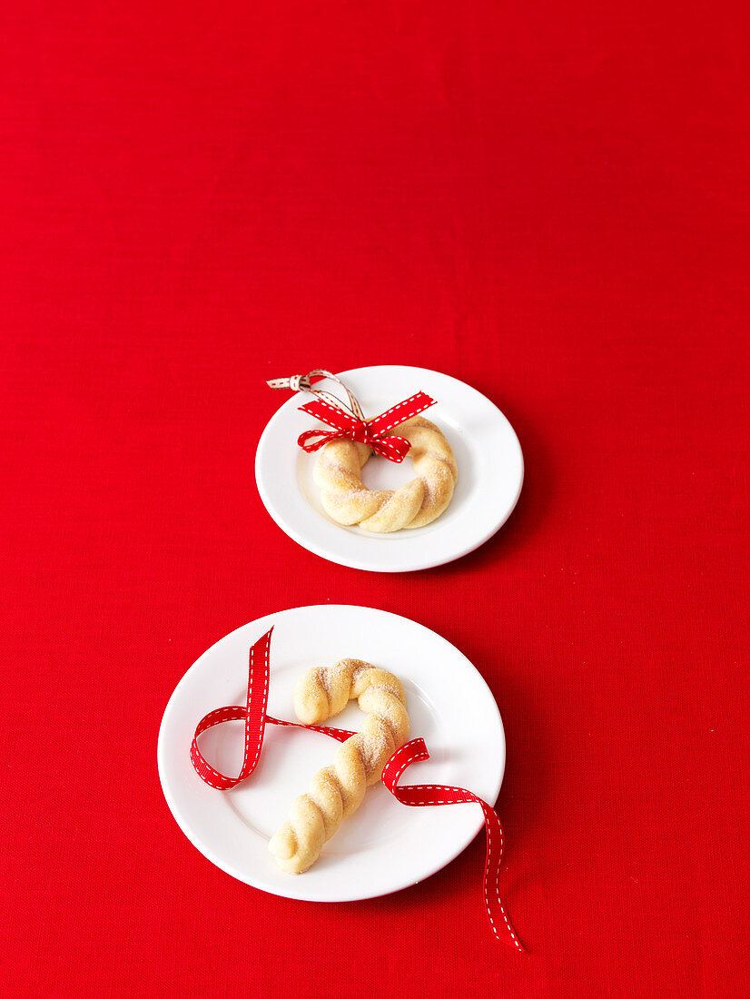Weihnachtsplätzchen mit Dekoband auf weißem Teller, auf rotem Untergrund
