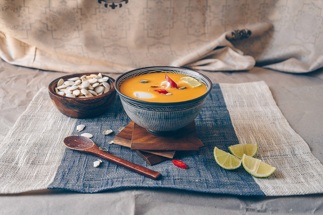 Spicy asian pumpkin soup garnished with red chillies, limes, and pumpkin seeds, topped with coconut cream