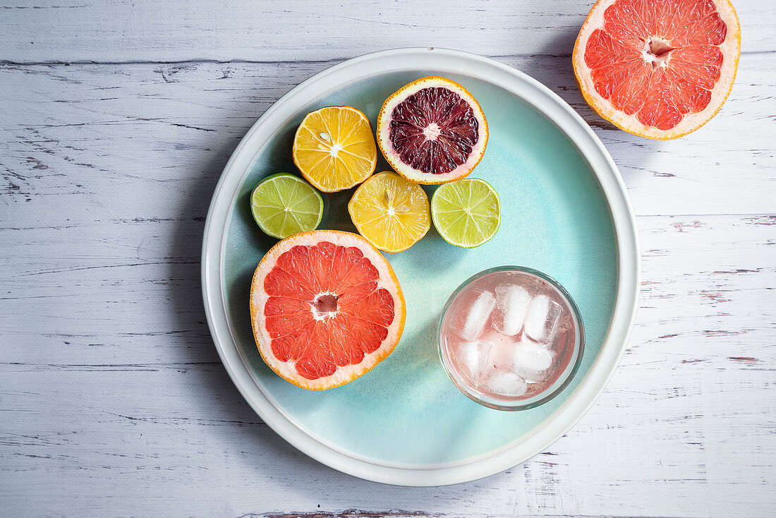Halved citrus fruits, a glass of grapefruit infused water with ice on a blue plate