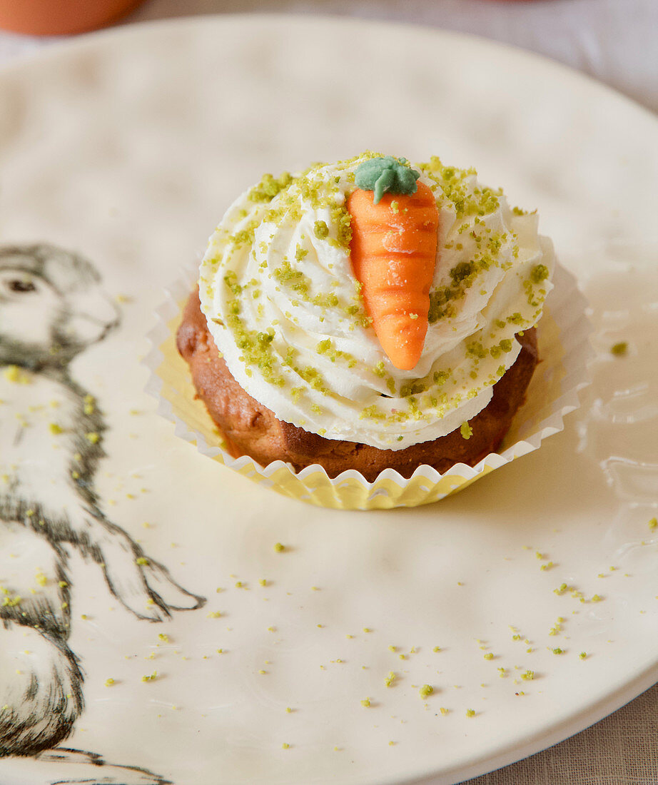 A carrot cupcake with butter cream, pistachios and a marzipan carrot