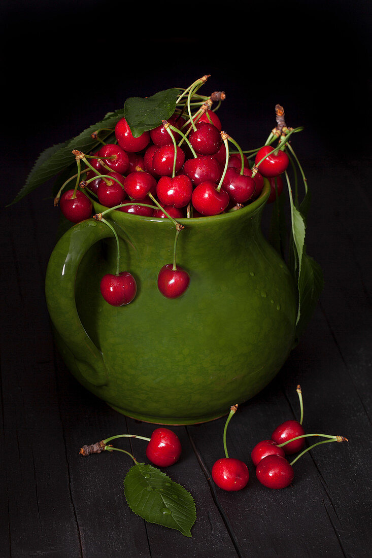 Ripe cherries in ceramic pitcher on black background