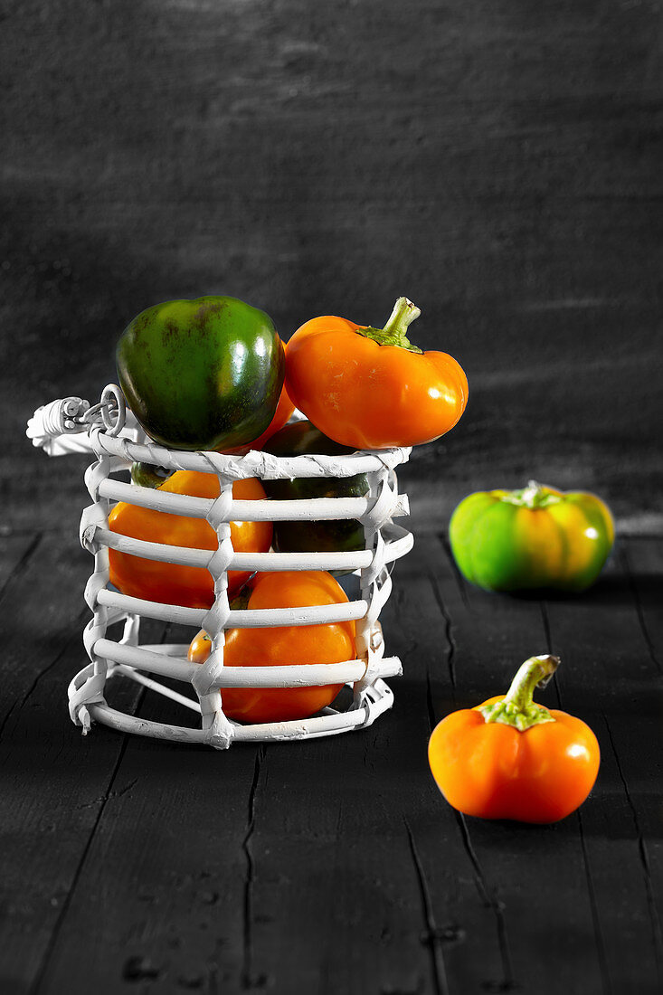 Yellow and green Hungarian tomato peppers in white basket, on black wooden background