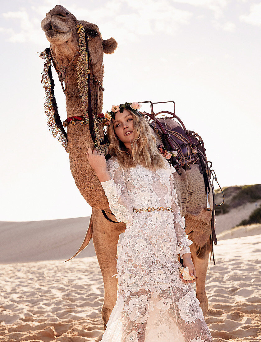 A young woman wearing a long white wedding dress with a camel