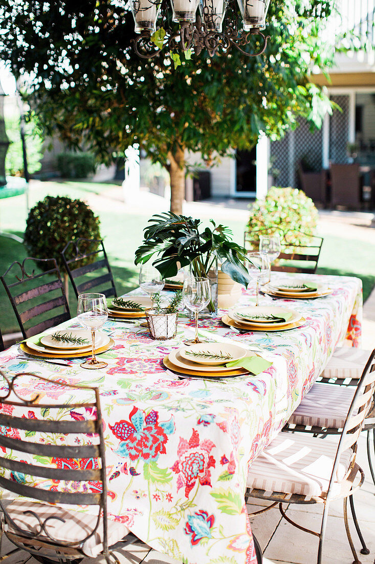 Gedeckter Tisch mit geblümter Tischdecke und Blätterzweig im Freien