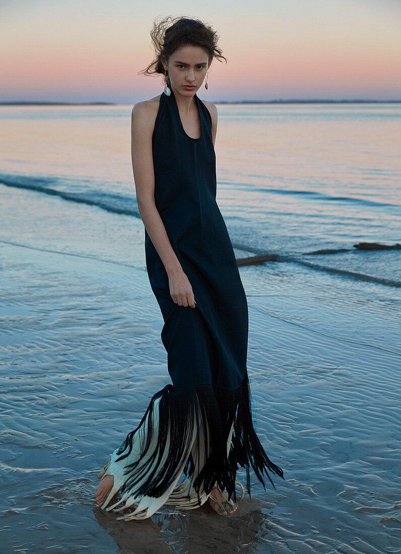 A dark-haired woman wearing a long black dress by the sea