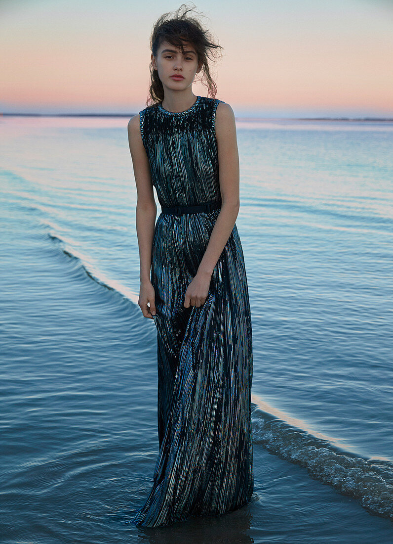 Dunkelhaarige Frau in langem, Abendkleid bei Sonnenuntergang am Meer