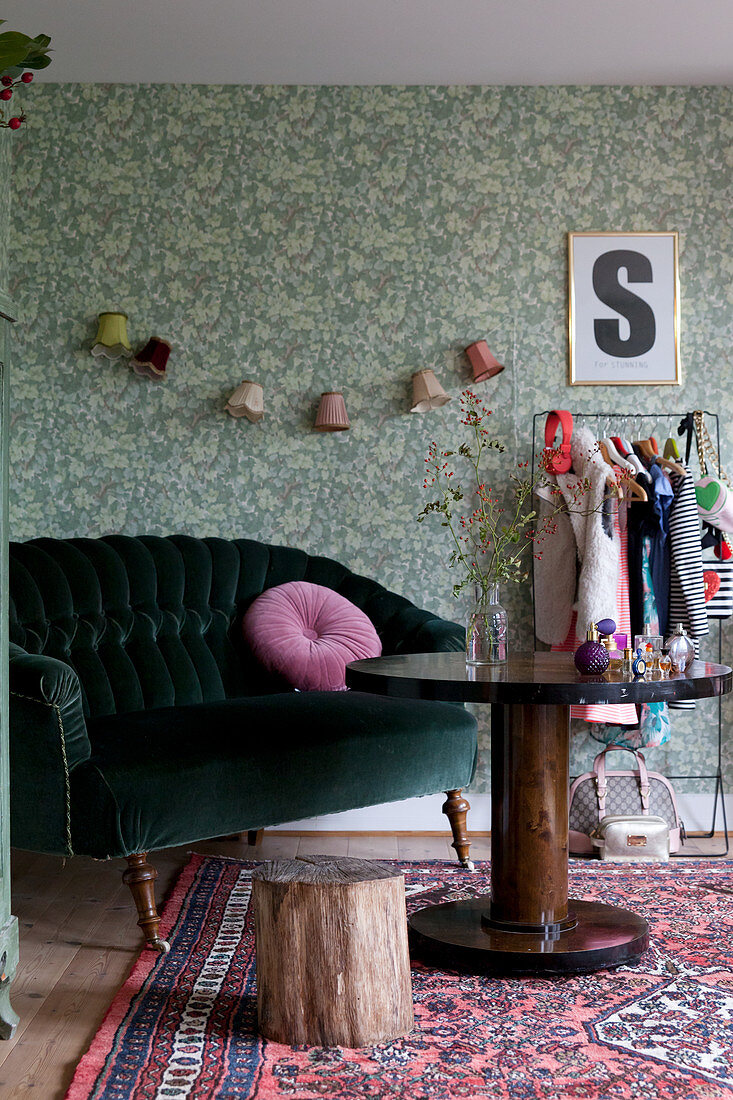 Green velvet sofa, round wooden table and green wallpaper