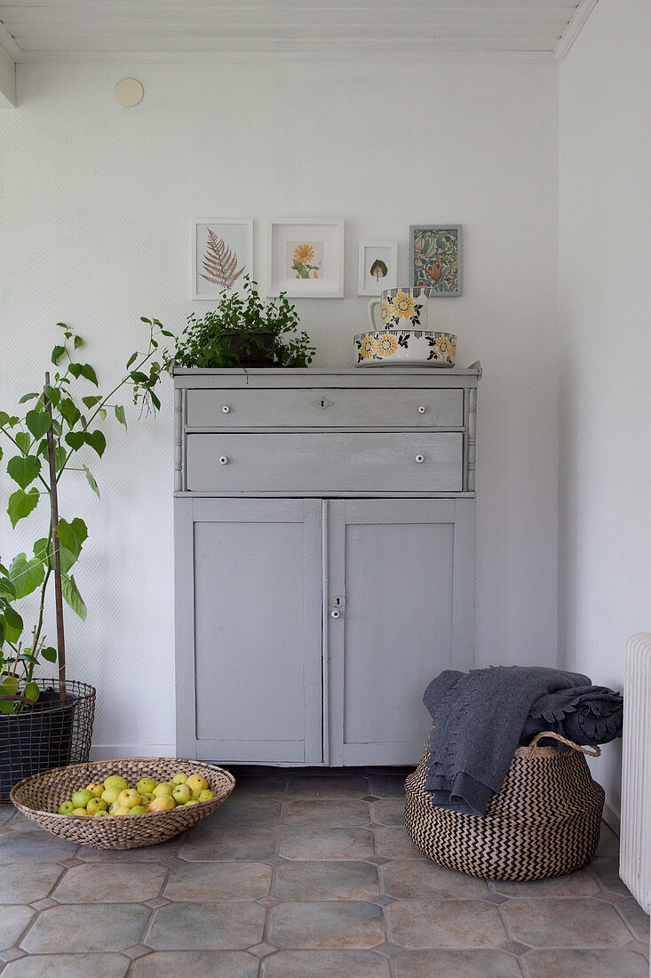 Grey cabinet, houseplants, shallow basket of apples and bag in foyer