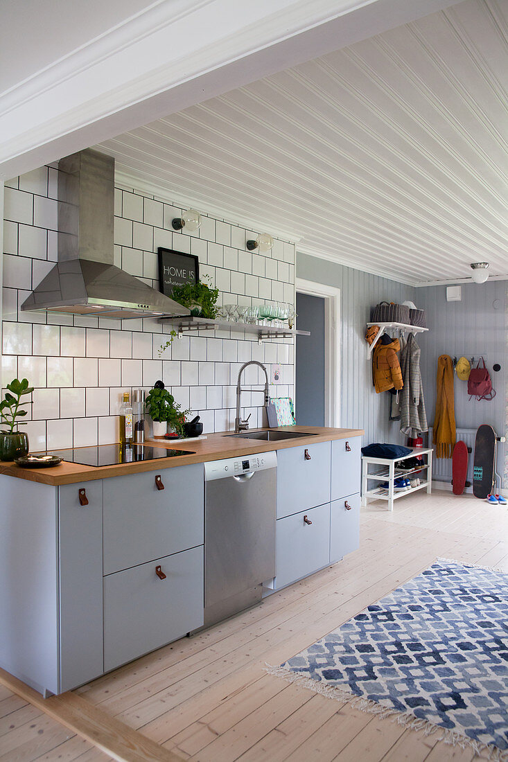 Grey kitchen counter against tiled wall, blue-and-white rug on pale wooden floor and coat rack in background