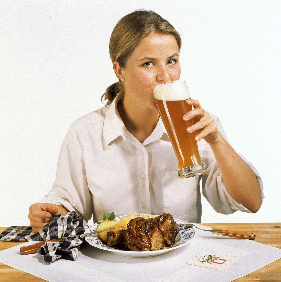 Modell vor Teller mit Schweinshaxe trinkt ein Glas Weißbier