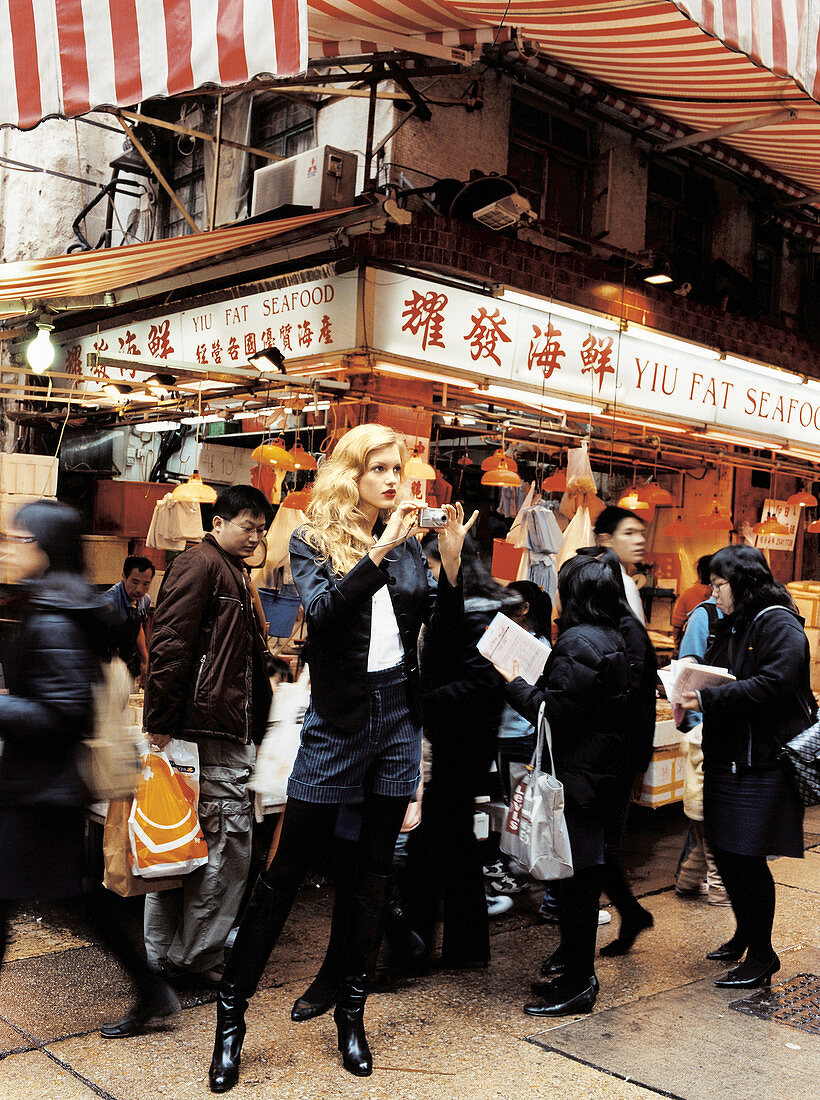 A young woman with a camera standing outside a Chinese restaurant in Hong Kong