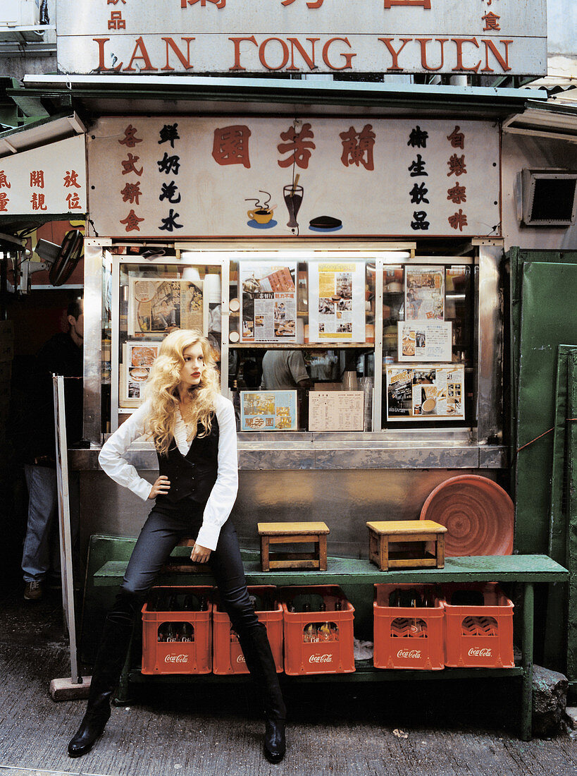 A blonde woman wearing a white shirt, a black waistcoat and black trousers standing outside a Chinese take-away