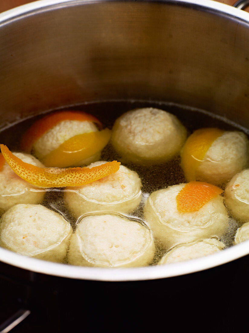 Quark dumplings being steeped in water with orange zest