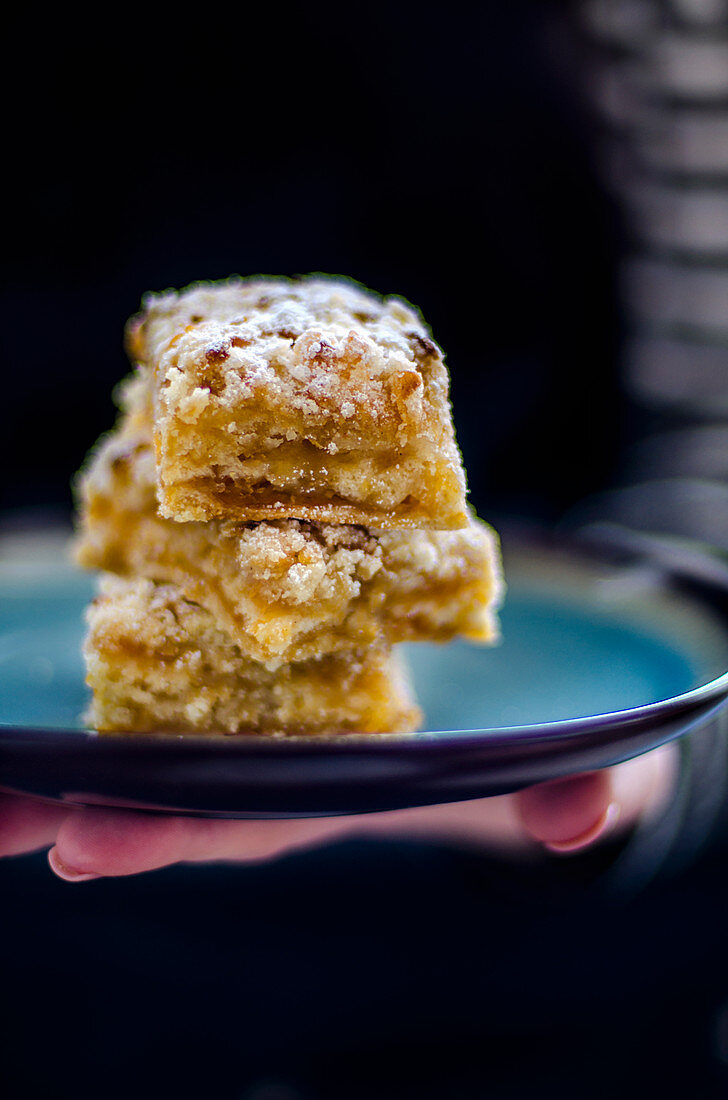 A hand holding three slices of apple crumble cake on a tray