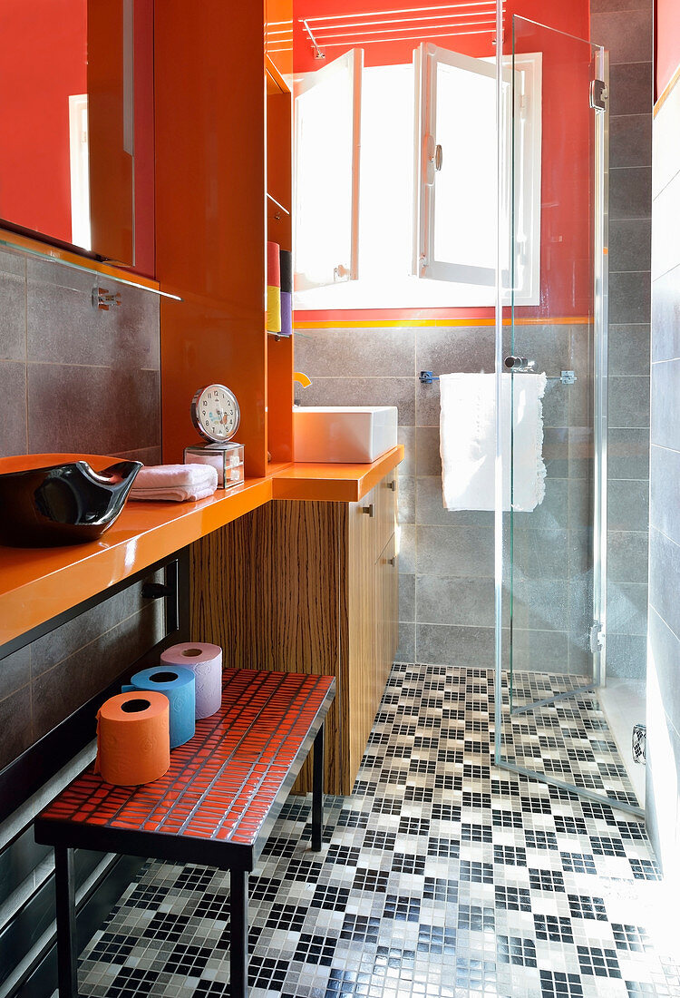 Toilet rolls on bench below washstand and shower cabinet with glass door in bathroom