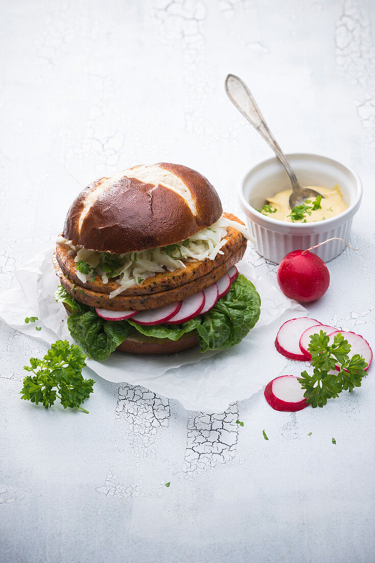 A lye bread roll with vegan meatloaf, coleslaw, radishes, lettuce and mustard