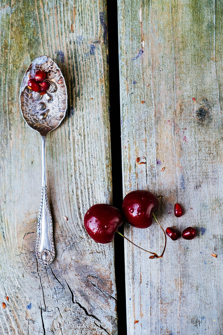 Cherries, pomegranate seeds and an old spoon on a wooden background