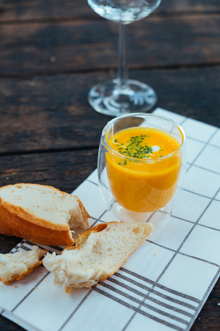 A glass of pumpkin soup next to a piece of white bread