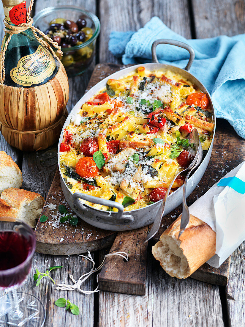 Pasta bake with tomatoes, olives, oregano and Parmesan with baguette and red wine