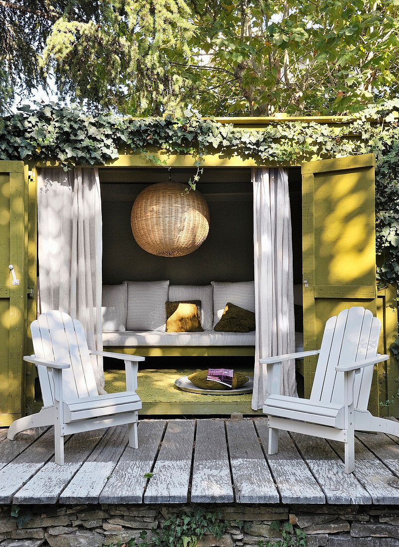 Two deckchairs on terrace outside climber-covered summerhouse